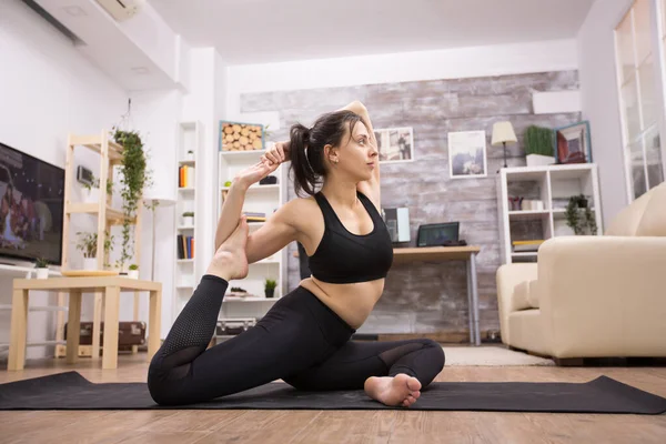 Pretty young woman in black sportswear doing one legged king pigeon yoga pose — Foto Stock