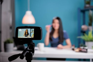Atractive influencer recording makeup tutorial showing cosmetic brush