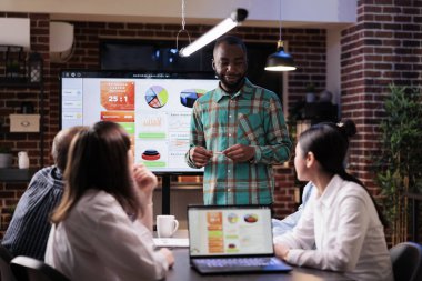 Afrika kökenli Amerikalı iş arkadaşı çeşitli takımlarla konuşuyor. Gece geç saatlerde yapılan toplantıda pazarlama fikirlerini tartışıyorlar.