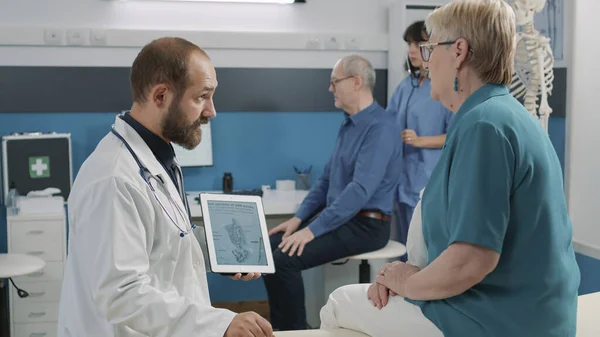 Male osteopath showing human skeleton illustration on tablet — Stock Photo, Image