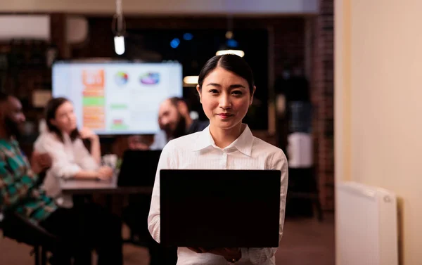 Retrato del trabajador de oficina asiático sonriente sosteniendo el ordenador portátil en la oficina de negocios durante la reunión nocturna — Foto de Stock