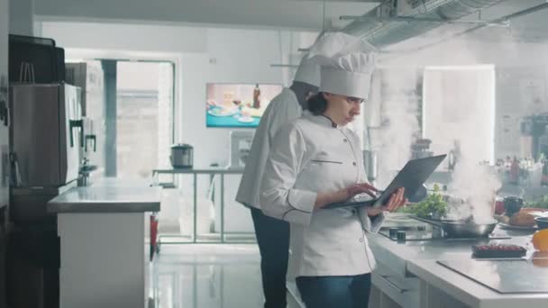 Vrouwelijke kok studeren professioneel voedsel recept op laptop — Stockvideo