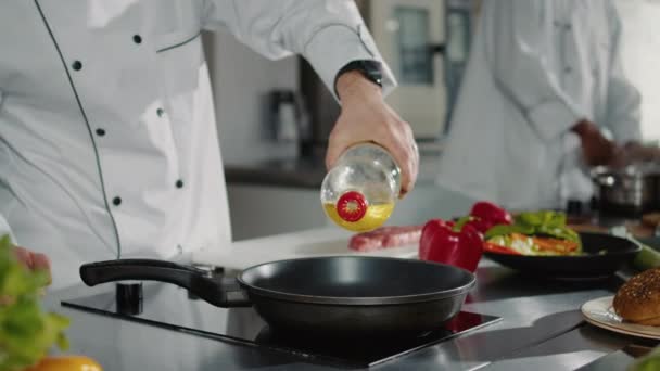 Чоловічий шеф-кухар, що поливає соняшникову олію з пляшки в сковороді на плиті — стокове відео