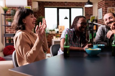 Oturma odasında oturup gülen ve şakalaşan çok kültürlü arkadaş grubu..