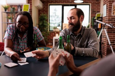 Diverse group of people sitting at home while playing charades card game together.