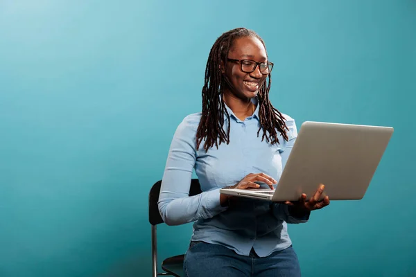 Joyful mooie vrouw met draagbare moderne computer staan op blauwe achtergrond tijdens het surfen web — Stockfoto