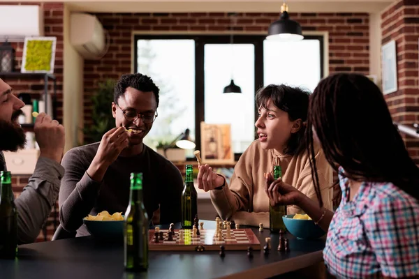 Χαρούμενη ομάδα φίλων που κάθονται στο τραπέζι στο σαλόνι, ενώ παίζουν επιτραπέζια παιχνίδια στρατηγικής μαζί. — Φωτογραφία Αρχείου