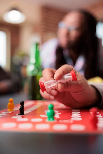 Close up shot of playful man holding boardgame hourglass in hand while sitting at table. — Foto de Stock