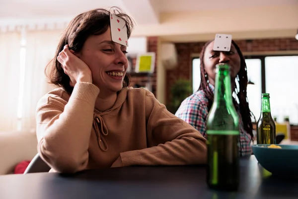Mujer sonriente con juego de cartas en la frente disfrutando de los juegos de la sociedad con amigos en casa. —  Fotos de Stock