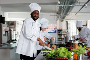 Afro-amerikan gastronomi uzmanı kendinden emin gülümserken akşam yemeği için taze sebze doğruyor ve kameraya poz veriyor.