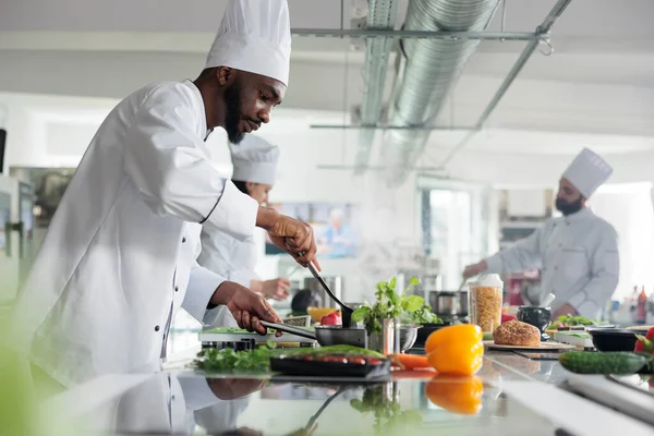 Experto gastronómico revolviendo con espátula en sartén mientras cocina delicioso plato para concurso de comida celebrado en el restaurante. — Foto de Stock