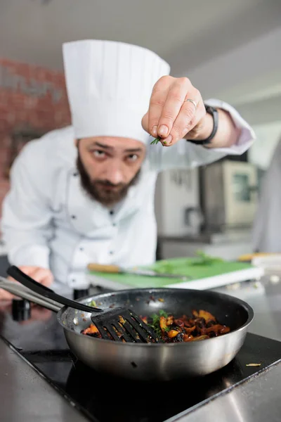 Gastronomia especialista jogando ervas frescas picadas na panela enquanto cozinha prato gourmet para o serviço de jantar no restaurante. — Fotografia de Stock