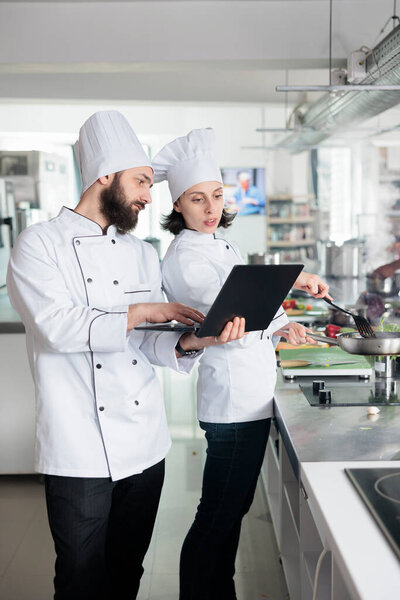 Gastronomy experts with laptop looking for gourmet dish recipe ingredients list