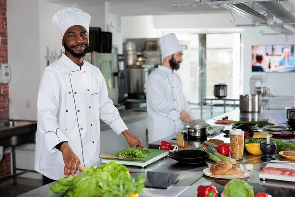 Afro-amerikan şef restoranda profesyonel mutfakta kameraya güvenle gülümsüyor..