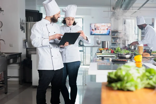 Expertos en gastronomía utilizando ordenador para decidir qué ingredientes utilizar para el evento gastronómico que se celebra en el restaurante. —  Fotos de Stock