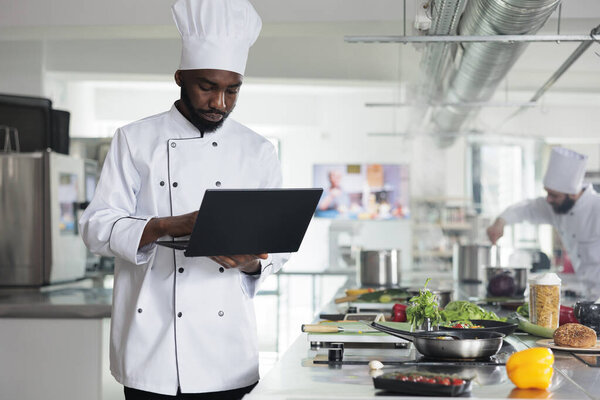 Professional cook wearing cooking uniform using computer to inspire for gourmet meal