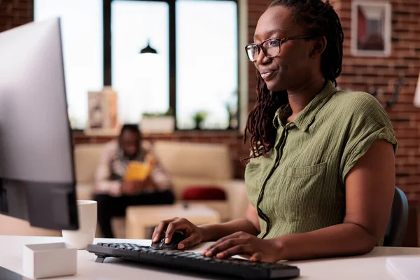 Focused african american programmer working remote from home while boyfriend is reading — 스톡 사진