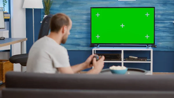 Man holding wireless controller playing console video game on green screen tv while sitting on sofa — Stock Photo, Image