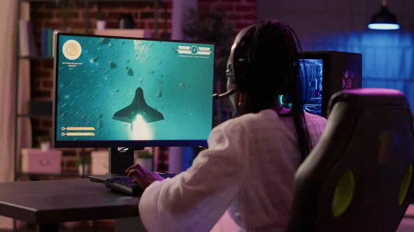 Sobre ombro vista de Africano americano gamer menina jogando espaço shooter simulação usando configuração de jogos pc — Fotografia de Stock