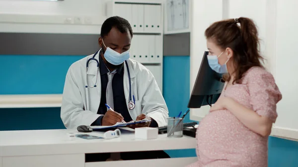 Medyk i oczekująca kobieta z maską do twarzy rozmawiająca o opiece zdrowotnej — Zdjęcie stockowe