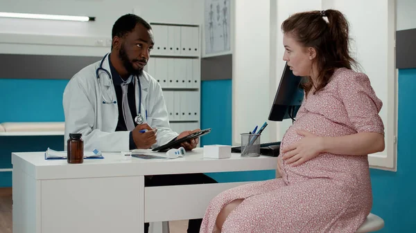 Especialista em maternidade tomando notas sobre tablet digital no check-up — Fotografia de Stock