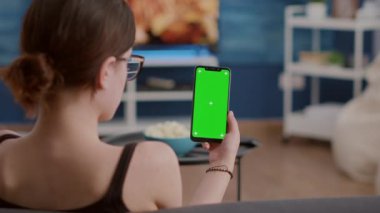 Yeşil ekranlı dikey akıllı telefonu olan genç bir kadının sosyal medya içeriğini izlediği yakın plan