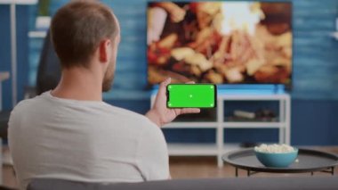 Çevrimiçi video içeriğini yeşil ekranlı akıllı telefonu tutan adamın yakın plan görüntüsü