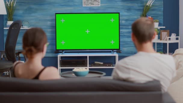 静的三脚ショットのカップル座っています上のソファ見ます上の緑の画面上のテレビリラックスした映画 — ストック動画