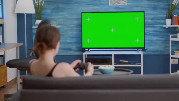 Молодая женщина держит беспроводной контроллер, играя экшн-консоли видеоигры на зеленом экране телевизора — стоковое видео