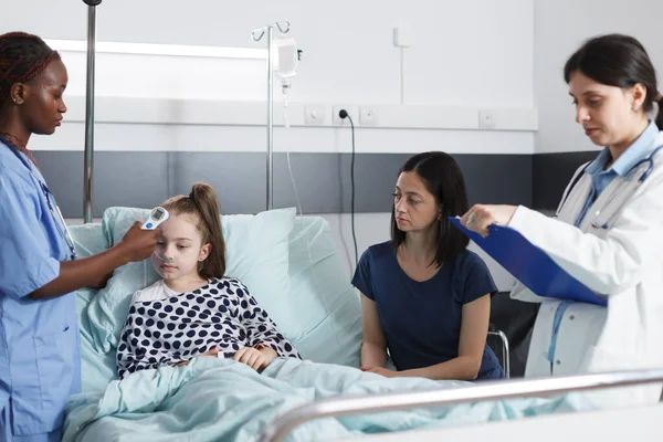 Enfermera médica midiendo la temperatura corporal de la niña enferma usando un termómetro moderno. —  Fotos de Stock