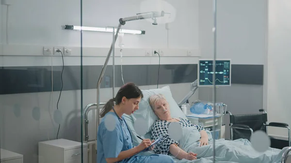 Medische assistent doet checkup bezoek voor patiënt in ziekenhuisafdeling bed — Stockfoto