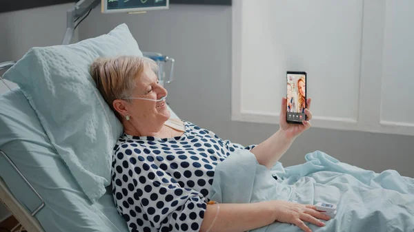 Paciente sênior conversando com a família em videochamada na enfermaria do hospital — Fotografia de Stock