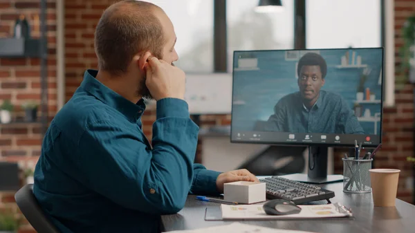 Muž používající sluchátka a video hovor na monitoru si popovídat s kolegou — Stock fotografie