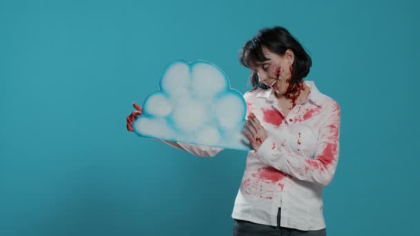 Inquietante zombie donna in possesso di cartone nuvola arte mentre in piedi su sfondo blu. — Video Stock