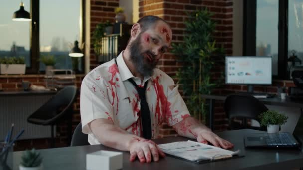 Griezelige zombie kantoormedewerker met diepe en bloederige gezichtswonden grijnzend bizar op camera. — Stockvideo