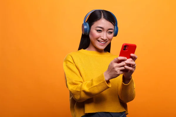 Calm peaceful young adult woman wearing headphones while using smartphone to enjoy funny online content.