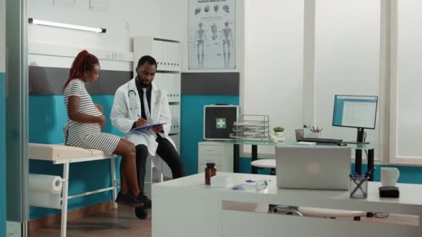Άντρας γιατρός κρατώντας σημειώσεις κατά το check up επίσκεψη με έγκυο γυναίκα — Αρχείο Βίντεο