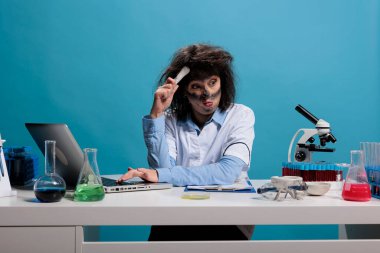Kimyasal deneylerin neden patlamaya yol açtığını anlamaya çalışırken kafasını kaşıyan aptal biyokimya uzmanı. Kafası karışmış çılgın bilim adamı laboratuvarda masasında oturuyor..
