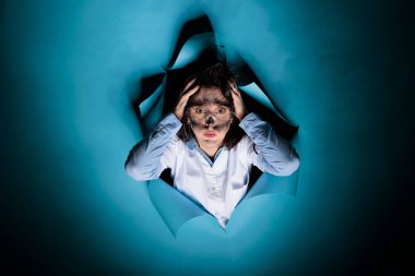 Tuhaf görünüşlü çılgın bilim adamı başarısız kimyasal deneylerden sonra ellerini başının üstüne koyuyor. Mavi arka plandaki laboratuvar patlamasından sonra dağınık saçlı, deli bir kimyager..