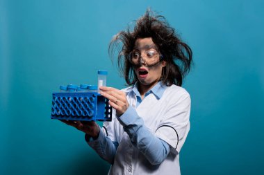 Plastik test tüpünde etiketi okurken şaşırmış gibi davranan aptal profesyonel bir laboratuvar çalışanı. Çatlak, komik bilim adamı başarısız kimyasal deneyin nedenini anlayınca çok şaşırdı..