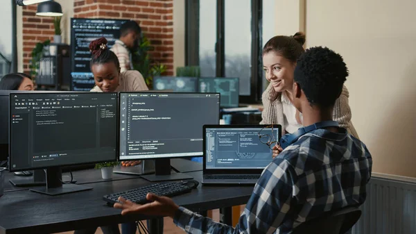 Software developers celebrating successful code compiling doing high five hand gesture with colleague. Programmer analyzing algorithm on multiple screens takes off glasses and congratulates coworker.