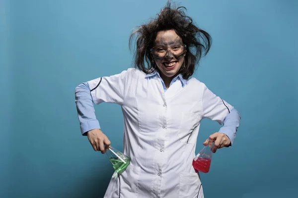 疯狂的生化专家一边笑着 一边拿着装满液体物质的艾伦迈耶烧瓶 面色苍白 头发凌乱 神智不清的疯狂化学家 背景是蓝色的 — 图库照片