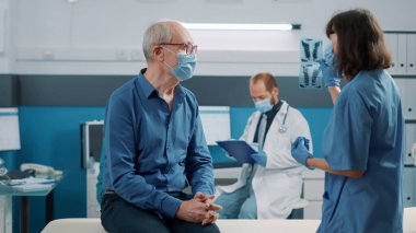 Kabinede yaşlı bir adama radyografi taraması yapan kadın hemşire. Röntgen sonuçlarına bakan kıdemli hasta ve uzman, hastalıkları tedavi etmek için tıbbi yardım ve destek alıyorlar..