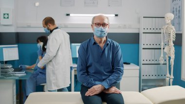 Coronavirus salgını sırasında tıp kabinesinde doktorla görüşmek için bekleyen yaşlı adamın portresi. İyileşme için rehabilitasyon uzmanıyla sağlık kontrolüne katılan yaşlı bir hasta..