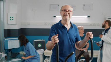 İyileşme ve rehabilitasyon için sabit bisiklet kullanan kıdemli bir hastanın portresi. Yaşlı adam fizyoterapi yapıyor ve mekanik bozuklukları tedavi etmek için alternatif ilaçlar deniyor..