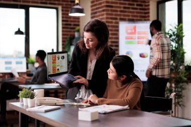 Çok ırklı ortaklardan oluşan bir ekip engelli ofisindeki dizüstü bilgisayarla ilgili raporları analiz ediyor, tekerlekli sandalyedeki felçli kişiyle çalışıyor. Fiziksel engelli Asyalı kadın iş planlama stratejisi.