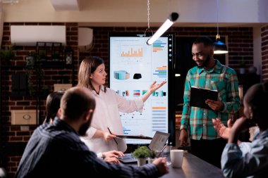 Kafkasyalı yönetici, yeni Afro-Amerikan meslektaşını sunuyor. Çeşitli takımlara pano tutuyor. Girişim sahibi iş arkadaşından pazarlama sunumunda satış grafiklerini sunmasını istedi.