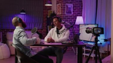 İnternet radyo sunucusu ev stüdyosunda dijital kamera kullanarak podcast yaparken yumruk tokuşturma hareketi yapan misafiri selamlıyor. Afrikalı Amerikalı podcaster ünlü bir konuşmacı ile röportaj yapıyor..