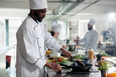 Afro-amerikan baş aşçısı restoranda akşam yemeği için yemek hazırlarken leziz etli köfte pişiriyor. Aşçı yamağı mutfakta et pişirirken lezzetli gurme yemekleri pişiriyor..