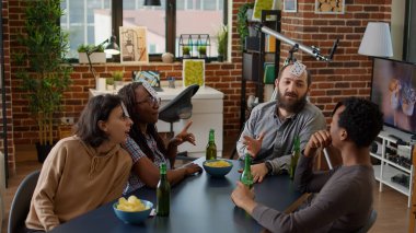 Oturma odasında stratejik kart oyunlarından hoşlanan çok ırklı bir grup insan parti toplantısında eğleniyor. Eğlence için rekabetçi aktivitelerle oyun oynayan mutlu arkadaşlar.